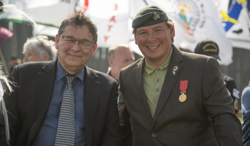 Two people smiling at the camera. The person on the right is wearing military clothing.